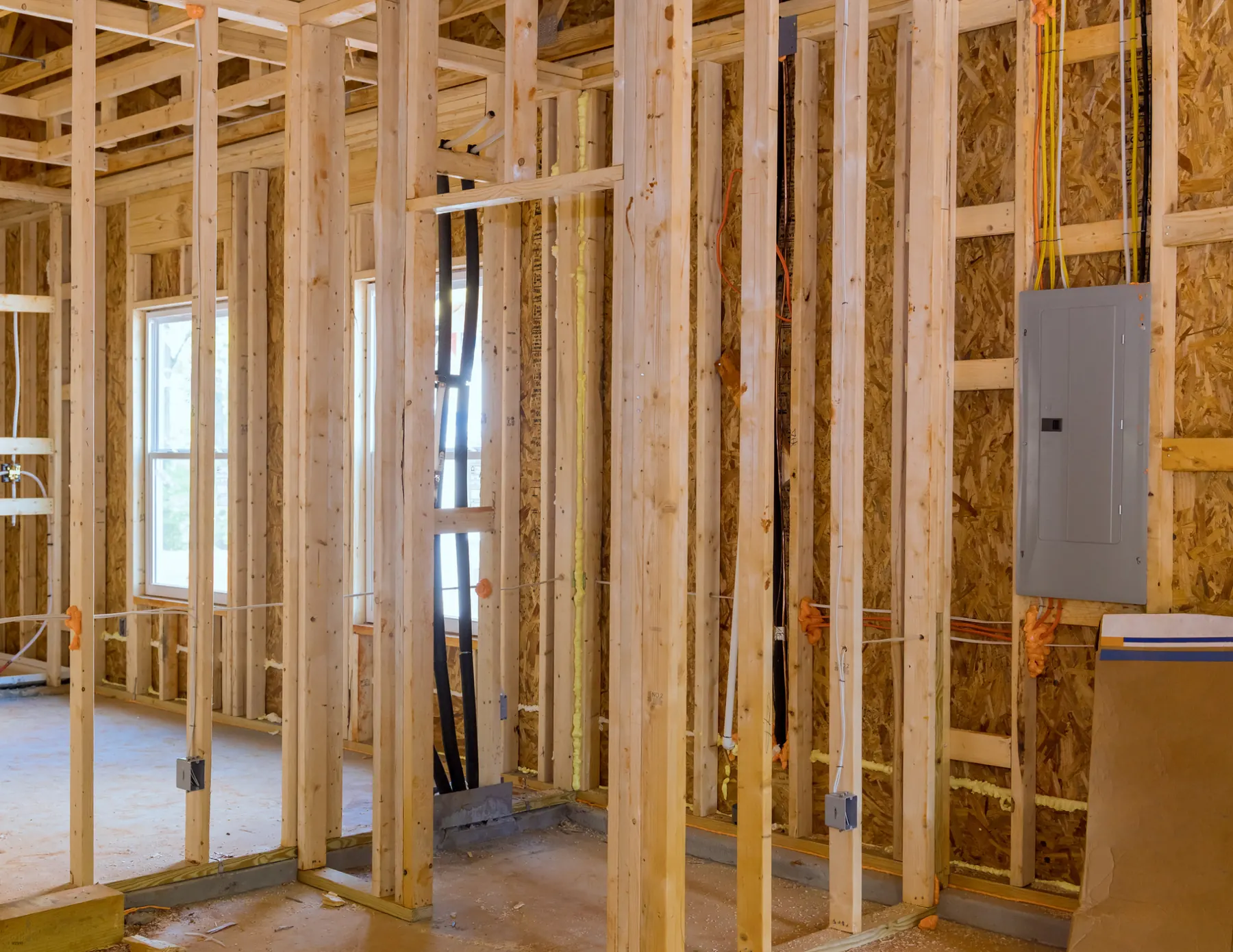 Wood-framed house interior before drywall, with the electrical panel and wiring exposed for as-built documentation